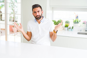 Handsome hispanic man casual white t-shirt at home clueless and confused expression with arms and...