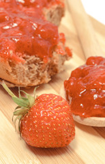 Strawberry jam on wooden spoon and wheat or rye bread in background