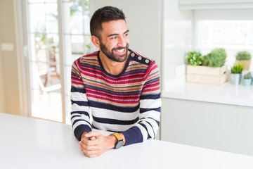 Handsome hispanic man wearing stripes sweater at home looking away to side with smile on face, natural expression. Laughing confident.