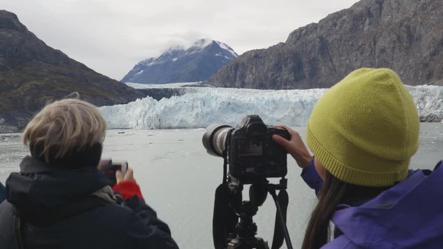 Alaska Glacier Bay Tourists looking at Margerie Glacier taking pictures on cruise ship using SLR camera and phone. People on vacation travel cruising famous destination.