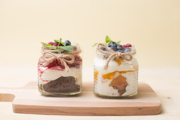 Raspberry cake in glass jar with fresh fruit and cream cheese on wooden background.