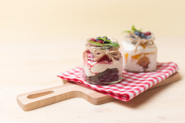 Raspberry cakes in glass jar with fresh fruit and cream cheese on a red napkin.