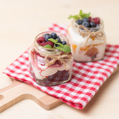 Raspberry cakes in glass jar with fresh fruit and cream cheese on a red napkin.