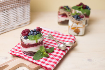 Raspberry cakes in glass jar with fresh fruit and cream cheese on a red napkin.