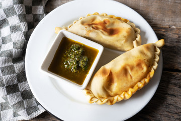 Argentine empanadas with chimichurri sauce on wooden background