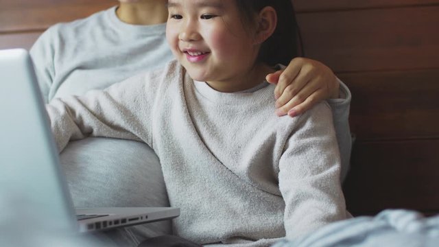 One happy little asian girl using laptop with her pregnant mother in the bed Chinese child learning to using computer with mom at home kid surfing the internet with parent