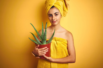 Young beautiful woman wearing a towel holding cactus pot over yellow isolated background with a confident expression on smart face thinking serious