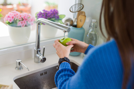 Young woman washing vegetables and fruit using water from sink