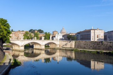 Fototapeta na wymiar St. Peter's Basilica and Emanuele II bridge with reflection in Tiber river at early morning.