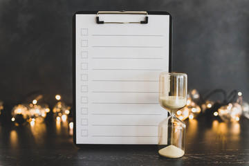 clipboard with blank list with cases to tick off on wooden desk with hourglass