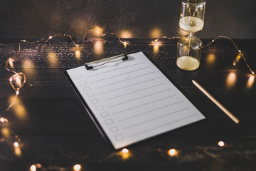 clipboard with blank list with cases to tick off on wooden desk with hourglass