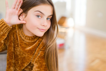 Beautiful young girl kid wearing casual sweater smiling with hand over ear listening an hearing to rumor or gossip. Deafness concept.