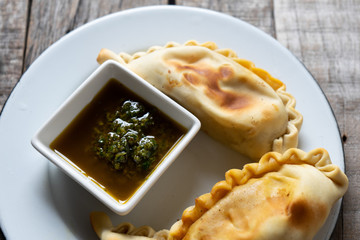 Argentine empanadas with chimichurri sauce on wooden background
