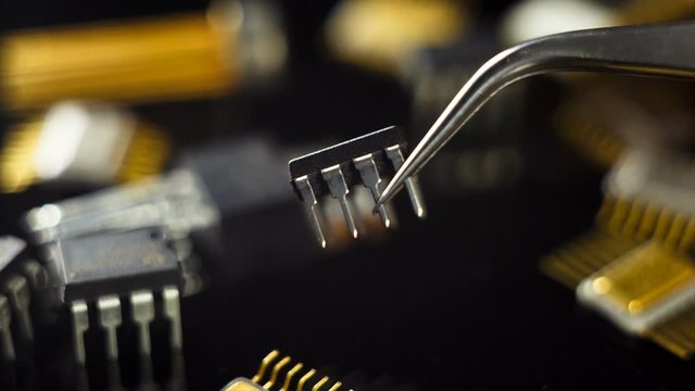 Microcircuit with tweezers on the background of electronic components.