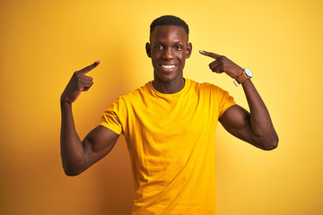 Fototapeta na wymiar Young african american man wearing casual t-shirt standing over isolated yellow background smiling pointing to head with both hands finger, great idea or thought, good memory