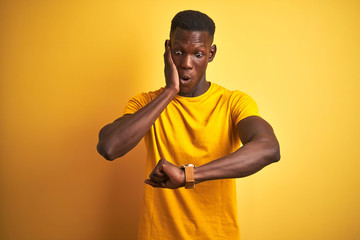 Young african american man wearing casual t-shirt standing over isolated yellow background Looking at the watch time worried, afraid of getting late