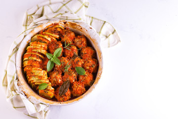 Homemade meatballs with tomato sauce in a white dish baked in the oven with herbs on marble white background