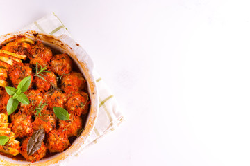 Homemade meatballs with tomato sauce in a white dish baked in the oven with herbs on marble white...