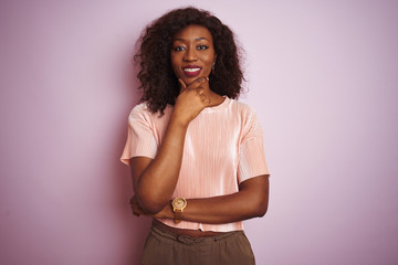 Young african american woman wearing t-shirt standing over isolated pink background looking confident at the camera smiling with crossed arms and hand raised on chin. Thinking positive.