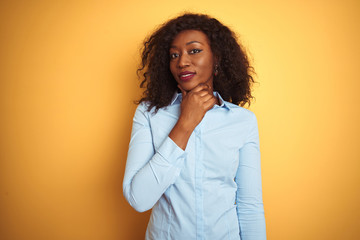 African american businesswoman wearing elegant shirt over isolated yellow background looking confident at the camera with smile with crossed arms and hand raised on chin. Thinking positive.