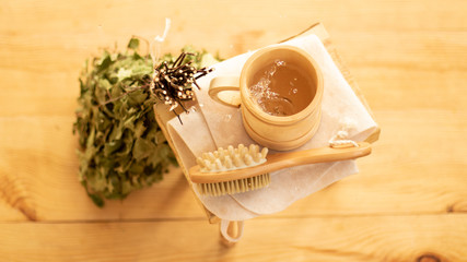 Pampering and relaxing in the sauna. Accessories for a steam room, wooden furniture, a bath broom and water in a mug.