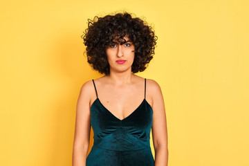 Young arab woman with curly hair wearing elegant dress over isolated yellow background skeptic and nervous, frowning upset because of problem. Negative person.