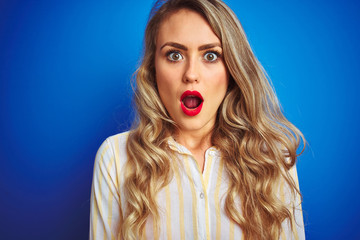 Young beautiful woman wearing striped shirt standing over blue isolated background scared in shock with a surprise face, afraid and excited with fear expression