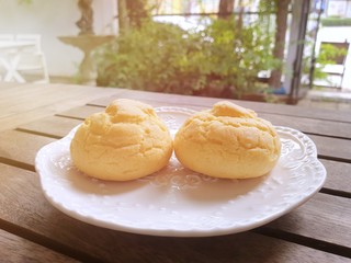Selective focus of Choux cream in white plate on wooden table with sun shining in café ready to eat (chu cream, Eclaire Vanilla cream, cream puff), Copy space