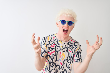 Young albino blond man wearing colorful t-shirt and sunglasses over isolated red background crazy...