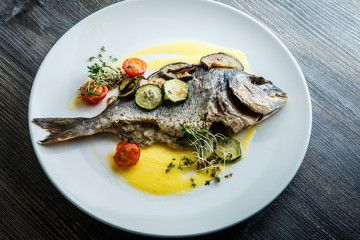 closeup oven baked fish served with sliced baked vegetables