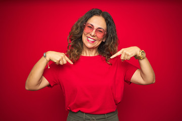 Middle age senior woman wearing cute heart shaped glasses over red isolated background looking...