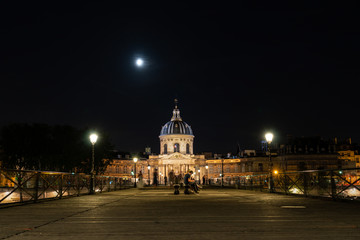 Institut de France and people walking on Pont des Arts at night - Paris, France.