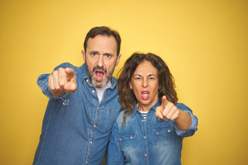 Obraz premium Beautiful middle age couple together standing over isolated yellow background pointing displeased and frustrated to the camera, angry and furious with you
