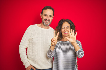 Naklejka premium Beautiful middle age couple wearing winter sweater over isolated red background showing and pointing up with fingers number seven while smiling confident and happy.