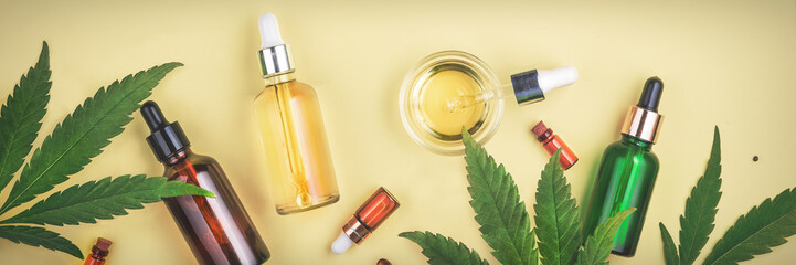 Different glass bottles with CBD OIL, THC tincture and cannabis leaves on yellow background. Flat...