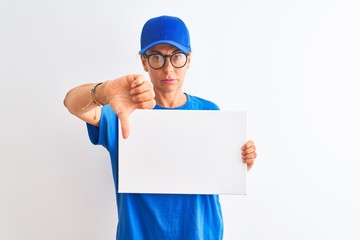 Senior deliverywoman wearing cap and glasses holding banner over isolated white background with angry face, negative sign showing dislike with thumbs down, rejection concept