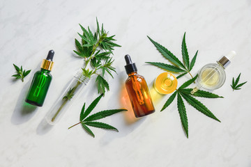 Various glass bottles with CBD oil, THC tincture and hemp leaves on a marble background. Flat lay,...