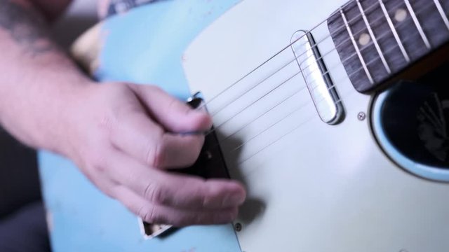 A man playing blue t-style guitar with pick.