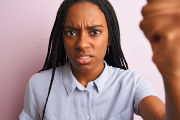 Young african american woman wearing striped shirt standing over isolated pink background annoyed and frustrated shouting with anger, crazy and yelling with raised hand, anger concept