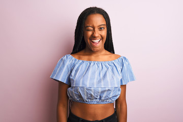African american woman wearing striped t-shirt standing over isolated pink background winking...