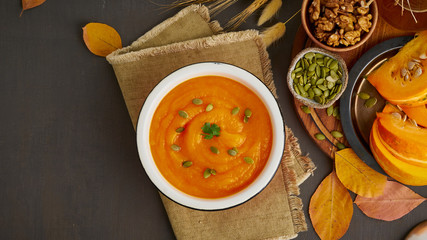 Banner of pumpkin cream soup with walnut and seeds, dark wooden background top view