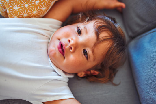 Beautiful toddler child girl wearing white bodysuit lying down on the sofa