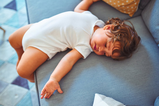 Beautiful toddler child girl wearing white bodysuit lying down on the sofa