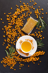 Obraz na płótnie Canvas Sea buckthorn, honeycomb with honey and cup of tea on black stone table.