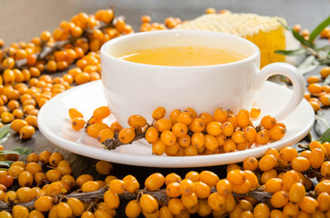 Sea buckthorn, honeycomb with honey and cup of  tea on black stone table.