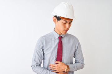 Chinese architect man wearing tie and helmet standing over isolated white background with hand on stomach because indigestion, painful illness feeling unwell. Ache concept.