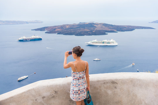 Europe travel tourist woman taking photo with phone of Mediterranean Sea in Santorini, Oia, Greece, with cruise ships sailing in ocean background.
