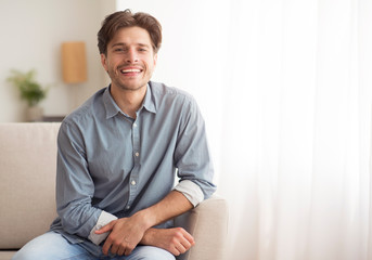 Fototapeta premium Young Man Smiling At Camera Sitting On Couch At Home
