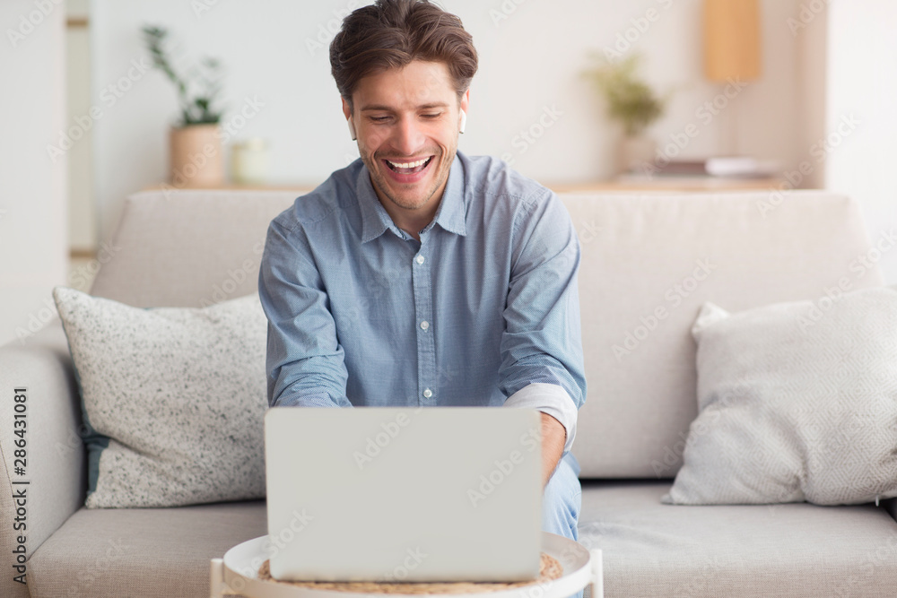 Poster smiling guy making video call via laptop sitting on couch