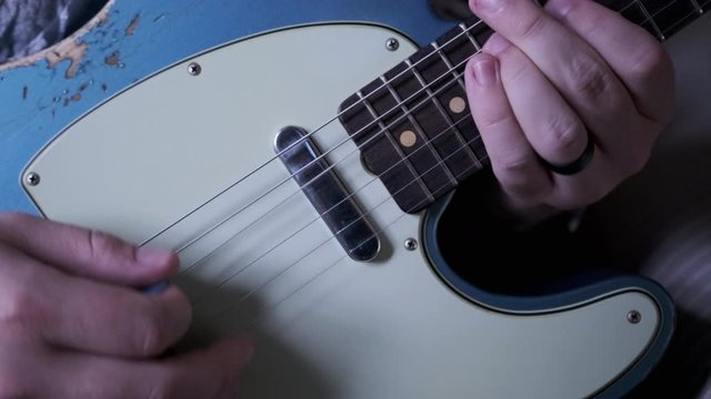 A man playing a blue t-style guitar higher up the neck.